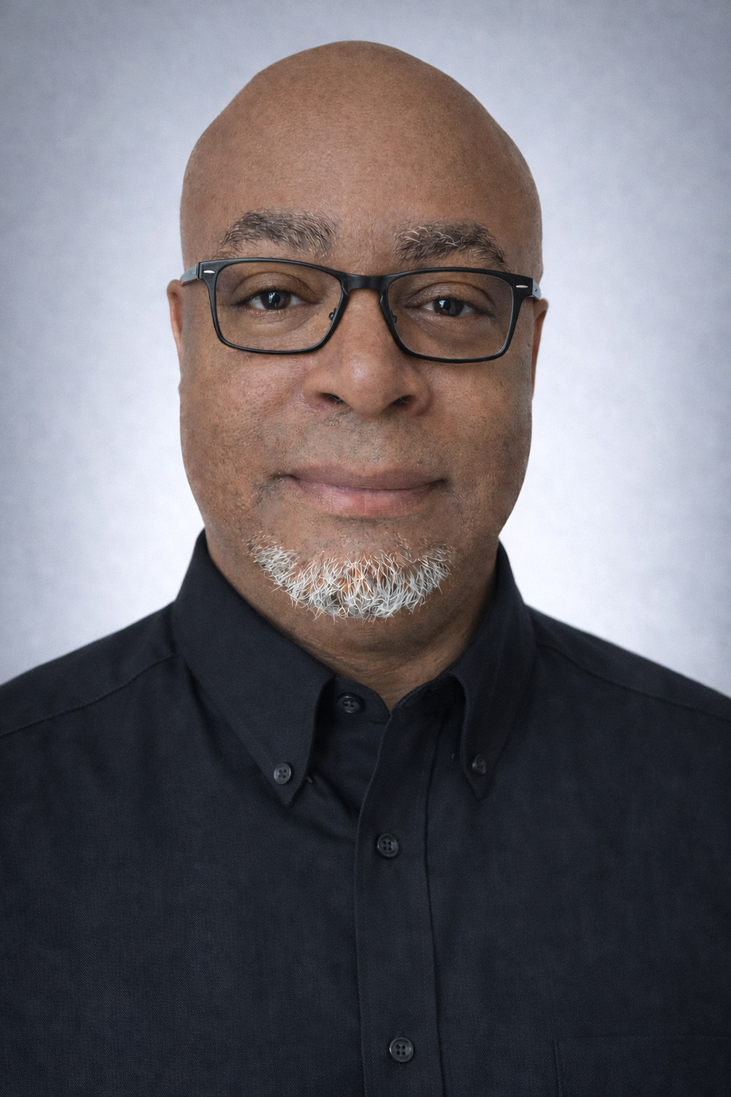 Close-up portrait of a man with a bald head and glasses, wearing a dark shirt, against a light background.